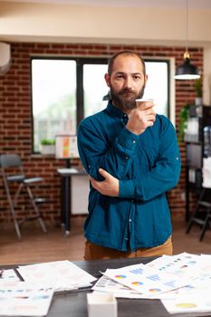 Portrait of bookkeeper man holding cup of coffee standing in startup company office