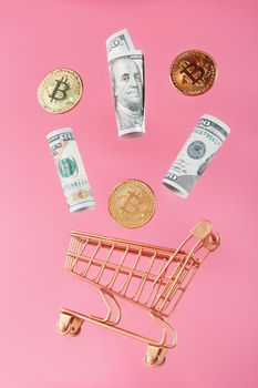 Gold mini cart with bitcoin coins and US dollars in a flight of levitation on a pink background.
