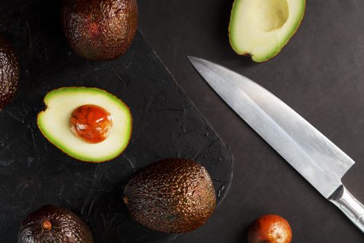 Sliced and whole organic avocado Hass with a knife on a black background.
