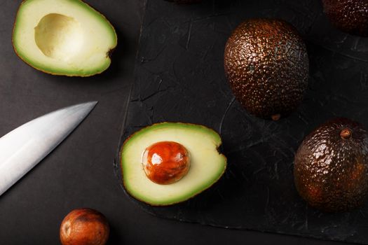 Sliced and whole organic avocado Hass with a knife on a black background.