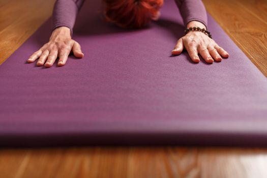 The girl does yoga in the asana stand on a lilac mat.
