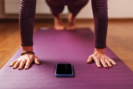 A girl does yoga with a smartphone in the asana stand on a lilac mat. Trainer, online training, online video yoga instructor, modern smartphone screen, meditation.