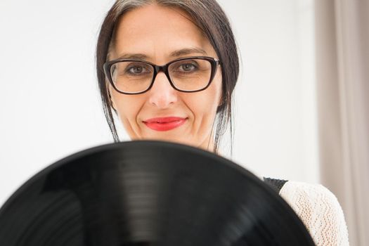 Studio photo of middle aged woman starting getting grey-haired wearing black and white clothes with vinyl record in hands on white background, middle age sexy lady, happy life concept