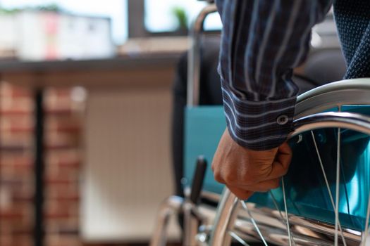 Closeup of startup employee hand holding rim of wheelchair wheel to move in front of desk