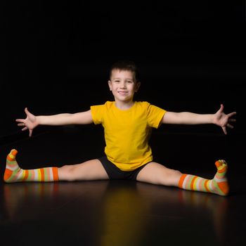 Boy sitting on floor with legs and hands wide apart