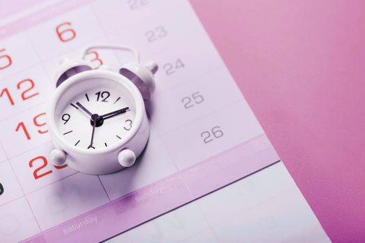 Calendar with a white alarm clock on a pink background.