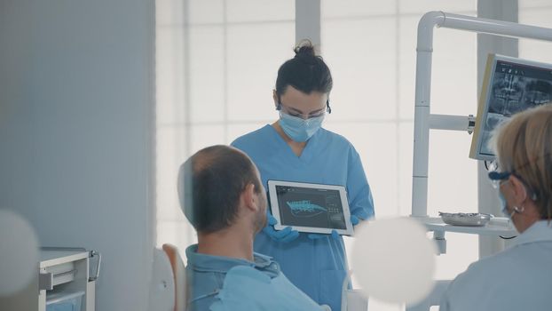Orthodontic nurse holding x ray results on tablet to show patient