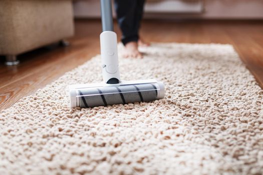 A cordless vacuum cleaner cleans the carpet in the living room with the bottom of the legs.