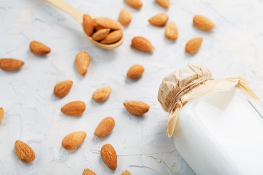 Almond milk in a glass bottle on a light background with a scattering of seed kernels and a wooden spoon.