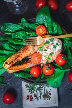 A plate with fresh green raw spinach and fried wild salmon, tomatoes and cream cheese sauce