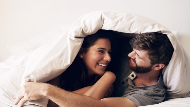 Make room for relaxation. Shot of a happy young couple covering themselves with a blanket on the bed at home.