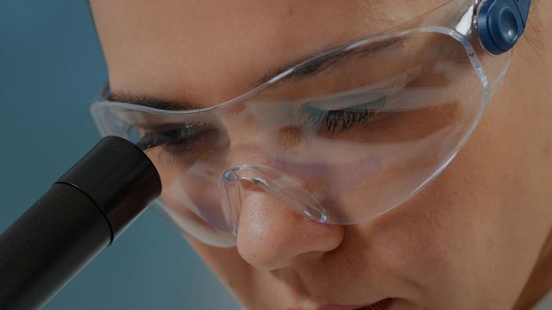 Woman chemist with protective glasses using microscope
