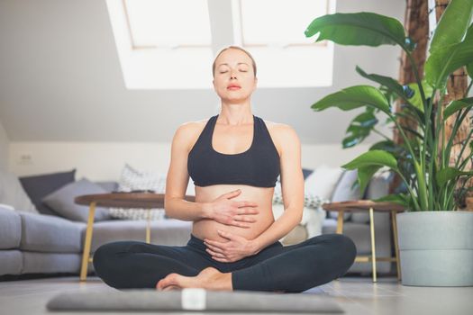 Young beautiful pregnant woman training yoga, caressing her belly. Young happy expectant relaxing, thinking about her baby and enjoying her future life. Motherhood, pregnancy, yoga concept.