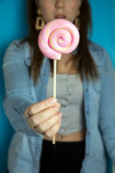 Happy beautiful woman giving colorful pink twirl lollipop on light blue background. Sweets,hard candy,gift,present concept