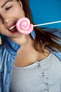 Portrait of a beautiful girl with colorful pink twirl lollipop hard candy on blue background, sweets,sugar and unhealthy food concept