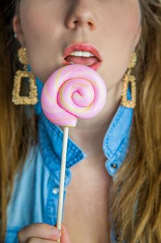 Portrait of a beautiful girl with colorful pink twirl lollipop hard candy on blue background, sweets,sugar and unhealthy food concept