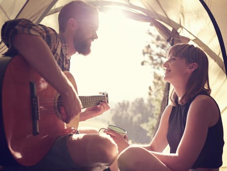 I wrote this just for you. Shot of a young man playing guitar to his girlfriend in a tent.