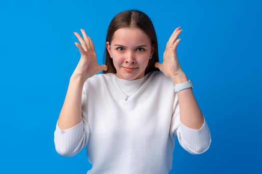 Young annoyed angry woman holding hands in furious gesture on blue background