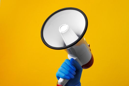 Human hand holding electronic loudspeaker against yellow background