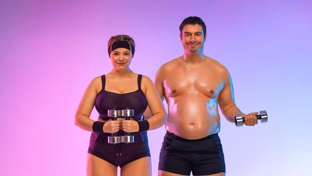 Fat man and woman in gym with dumbbells. Body positive and fitness concept.