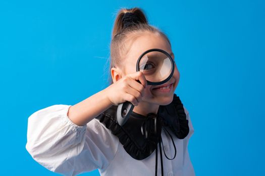 Little girl looking through a magnifying glass on blue background