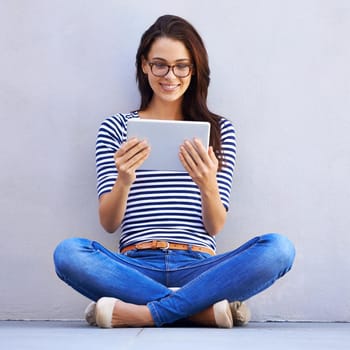 Living a digital lifestyle. Shot of an attractive young woman using a digital tablet while sitting cross-legged on the floor.
