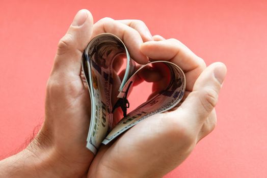 several 100 dollar bills folded in the shape of a heart in male hands. love of money, greed, business, wealth