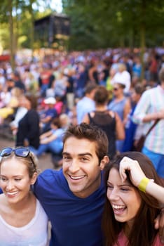 A group of smiling friends enjoying a music festival with crowd in the background