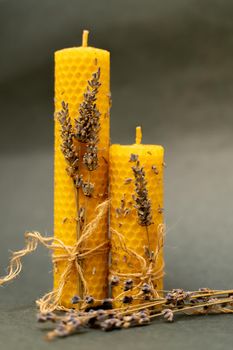 Two beeswax candles on a gray background. The candles are decorated with sprigs of lavender and tied with a jute rope.
