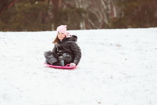 Happy little girl sliding down the hill on saucer sled. Girl enjoying slider ride on the snow
