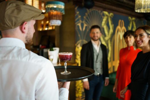 Waiter serving a cocktail for elegant guests in a nice bar