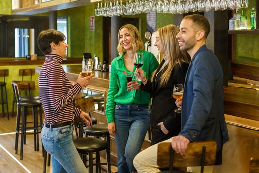 Gleeful diverse man and women with alcohol beverages smiling and talking while spending weekend day in bar together