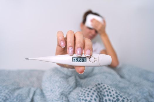 Sick woman with a high fever showing medical thermometer with temperature 38,2. Woman measuring body temperature
