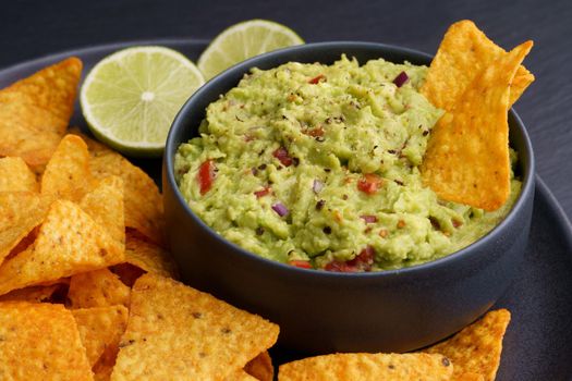 Guacamole dip with tortilla chips or nachos in black plate on a black background