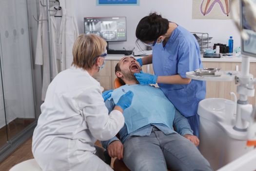 Dentist woman nurse checking patient mouth analyzing teeth infection using stomatological drill instrument during orthodontic examination in dental office room. Concept of dentistry procedure