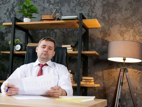 Tired employee works with financial statements. The man is holding a paper report.