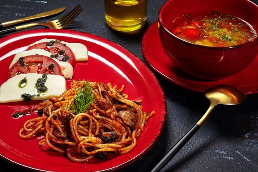 Set lunch from vegetable broth, spaghetti with mushrooms and Caprese salad