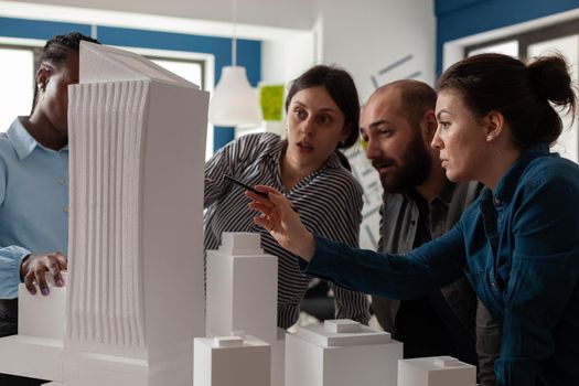 Professional architect with working partners pointing at skyscraper foam scale model