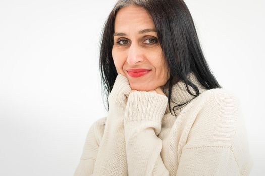 Middle aged woman starting getting grey-haired is posing in studio in sweater on white background, face skin care beauty, middle age skincare cosmetics, cosmetology concept