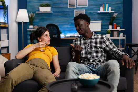 Cheerful interracial couple sitting on sofa in living room