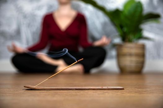 Mindful woman meditating at home with burning incense sticks, siting in lotus pose. Holding hands in lap with palms facing upwards.