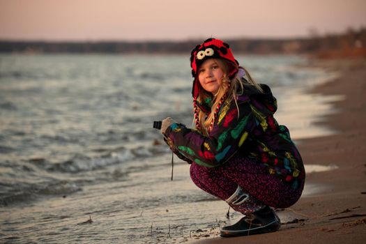 A 9 year old girls takes pictures with a camera at the beach at sunset.