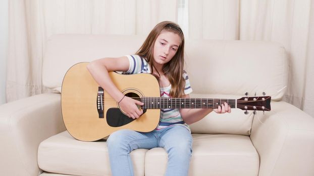 Young guitarist child sitting on sofa holding guitar learning how to sing