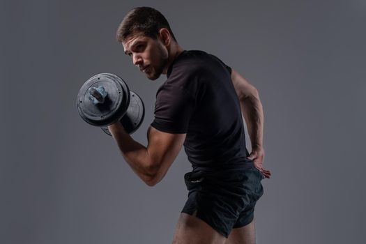 Focused strong guy performing bicep curls with dumbbell