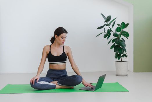 Young woman doing sports and yoga at home using a laptop. Advertisement for yoga courses