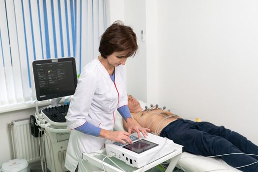 ECG concept. Woman doctor cardiologist doing electrocardiogram test to man patient in cardiology clinic. Medicine, cardiology, ECG of the heart concept. Male at medical testing