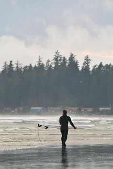 A Surfer Carries his Board Along the Beach in Tofino British Columbia in Canada