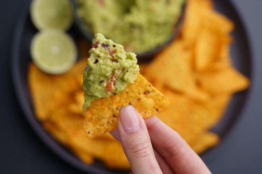 Closeup of woman hand holding guacamole and chips or nachos. Top view