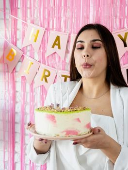 Beautiful woman celebrating birthday party holding a cake, blowing candles
