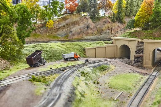 Miniature trucks with a train track, gravel road, and concrete overpass